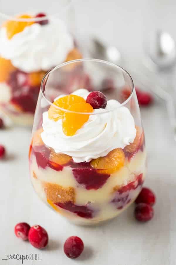 Vanilla cake, vanilla pudding, oranges and cranberry sauce layered together for the perfect holiday dessert -- this Cranberry Orange Trifle is great for potlucks! stemless wine glass filling with cranberry orange rifle topped with whipped cream mandarin orange slices and cranberry