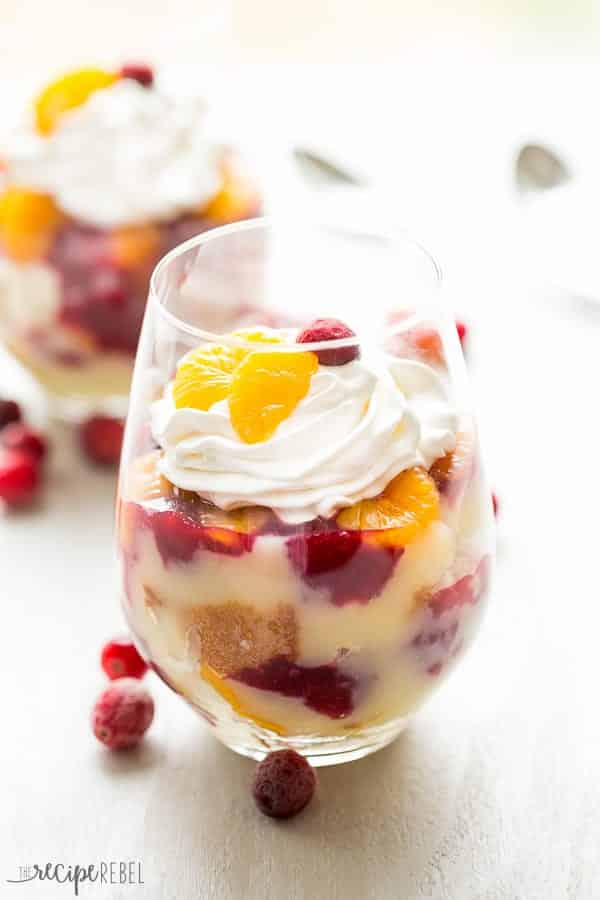 cranberry orange trifle in two stemless wine glasses topped with whipped cream mandarin oranges and cranberries