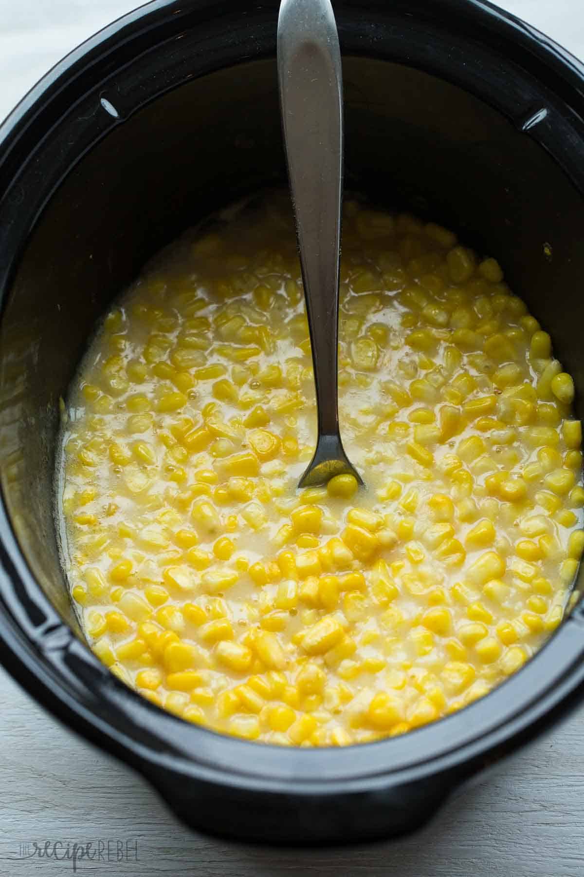 slow cooker creamed corn in black crockpot with spoon stuck in corn