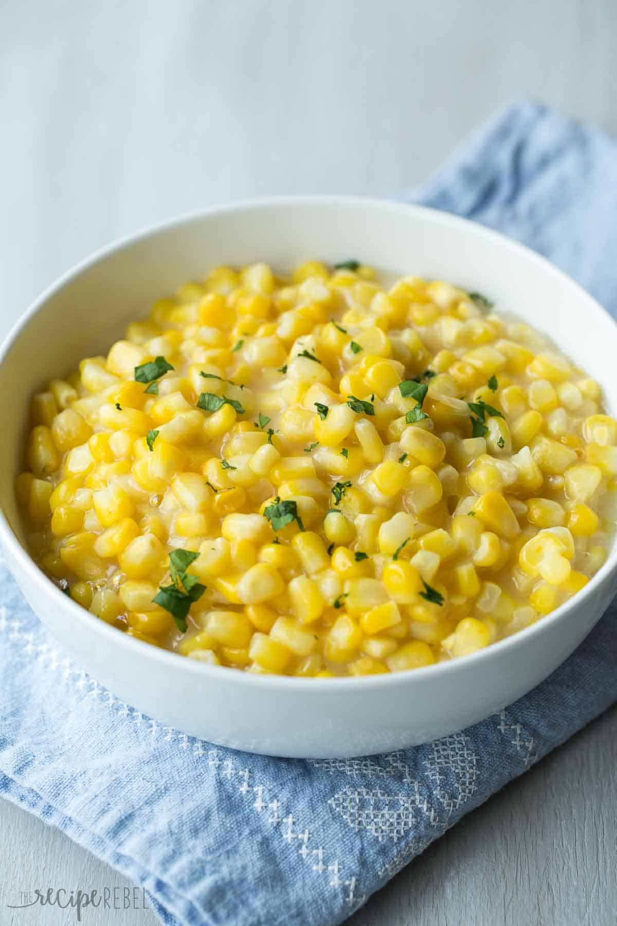 This Slow Cooker Creamed Corn is so easy -- just mix it together and throw it in! It has no cream and is a healthier, dairy free option that tastes just as good! white bowl with no cream creamed corn topped with chopped parsley