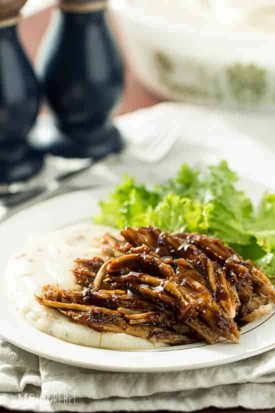 Tender, moist turkey breast brushed with a sweet and tangy apricot balsamic glaze -- the perfect slow cooker meal for the holidays so you can enjoy your guests! shredded turkey breast in apricot balsamic glaze on a bed of mashed potatoes on a white plate