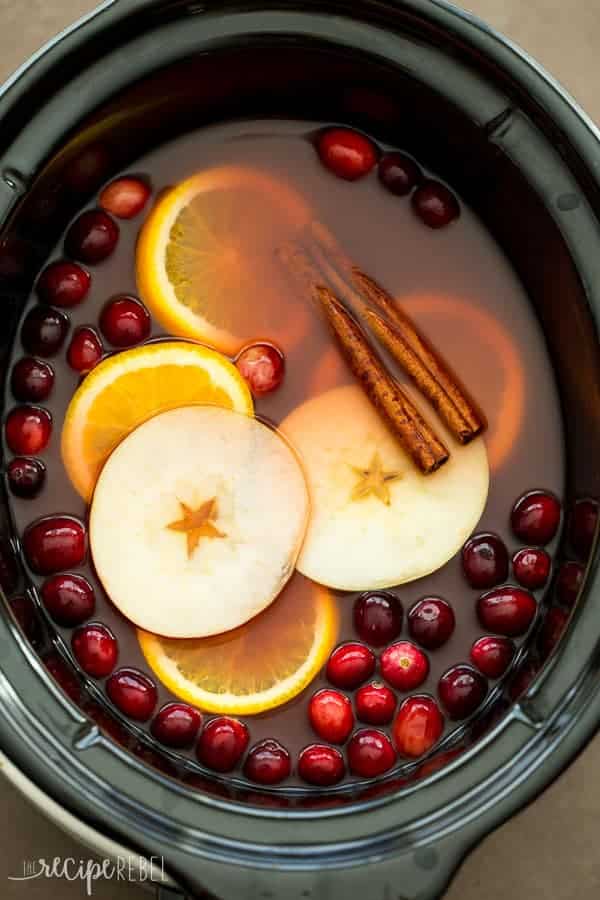 overhead image of slow cooker with cider in it and apple slices orange slices cranberries and cinnamon sticks for garnish