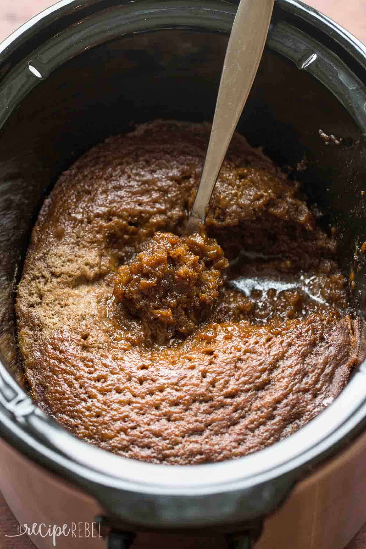 black slow cooker with gingerbread pudding cake in it and a metal spoon scooping some