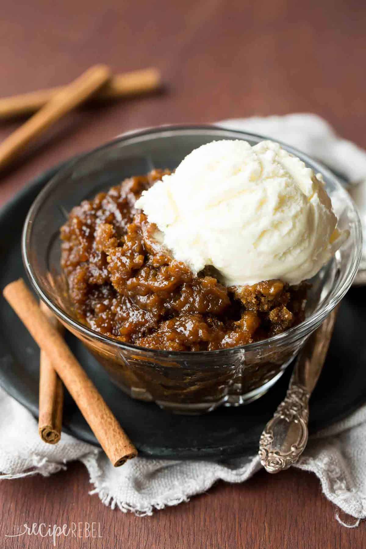 clear glass bowl full of gingerbread pudding cake topped with ice cream with cinnamon sticks on the side