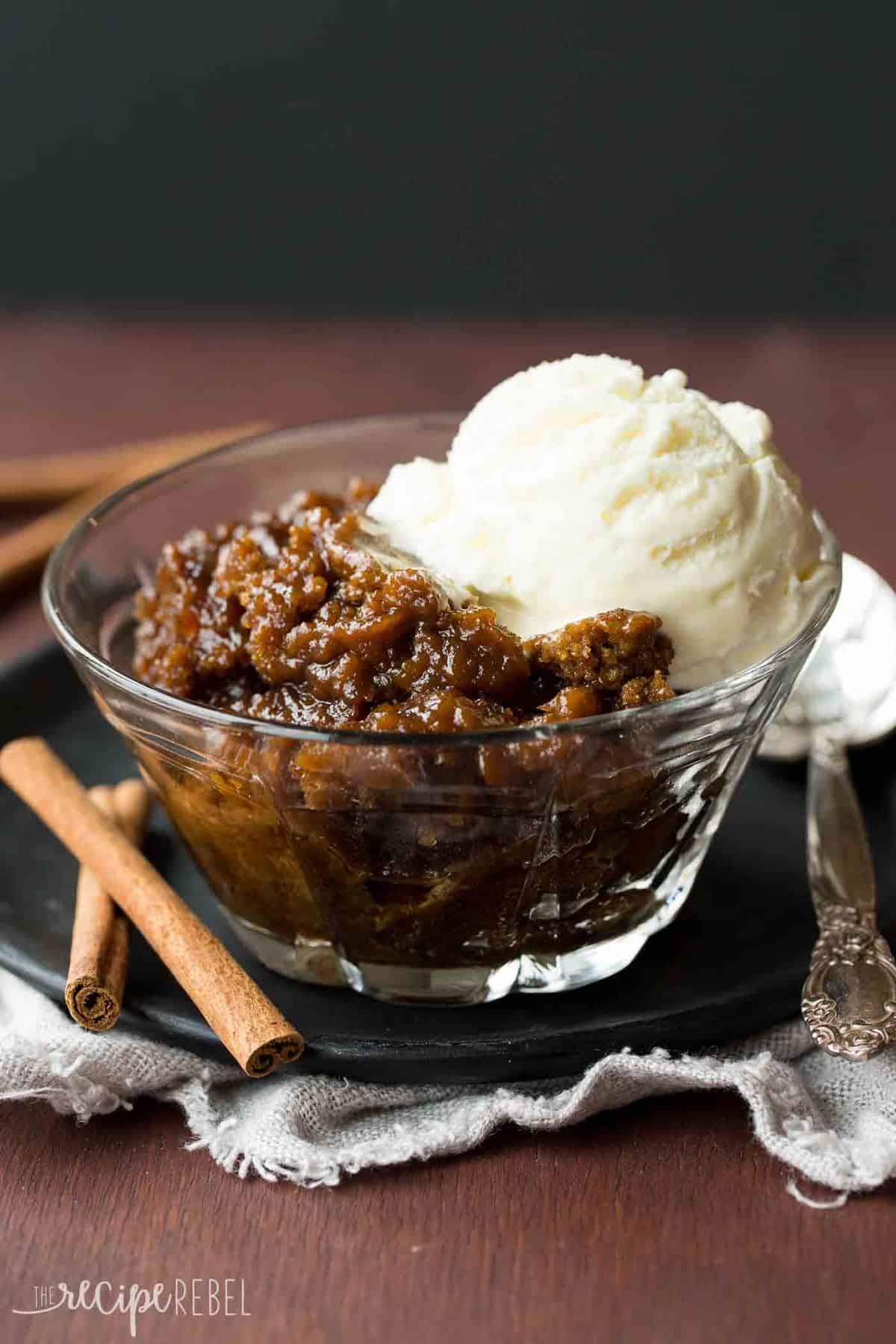 clear glass bowl of gingerbread pudding cake with scoop of vanilla ice cream on black plate
