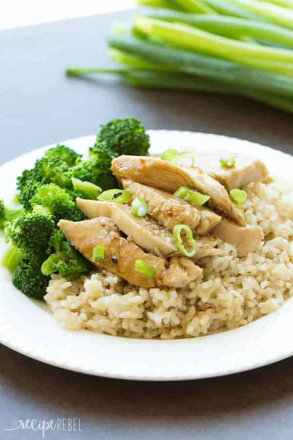 sliced chicken breasts on brown rice with broccoli on a white plate