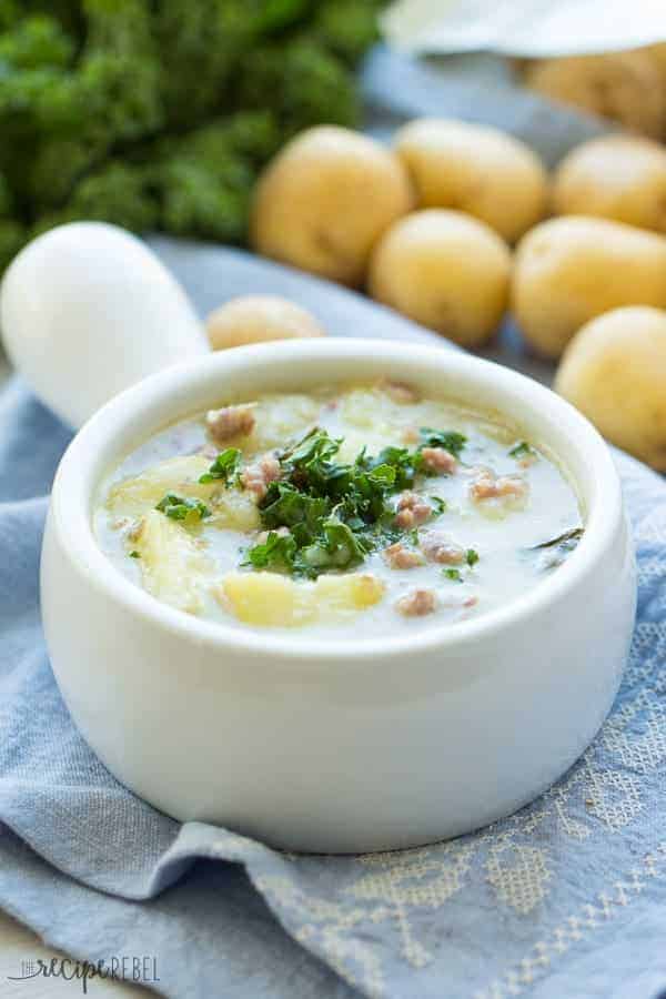 slow cooker zuppa toscana in white bowl with potatoes in the background