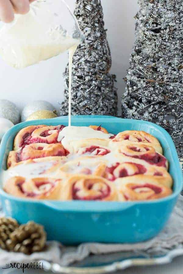 bright blue pan of cranberry sweet rolls with white chocolate glaze being poured over