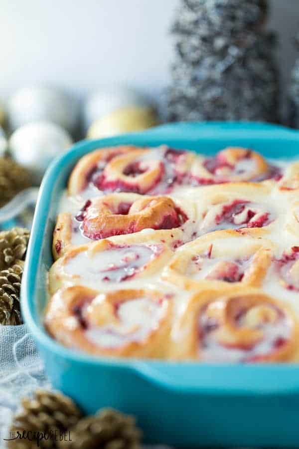 bright blue baking dish with cranberry white chocolate sweet rolls and christmas decor in the background