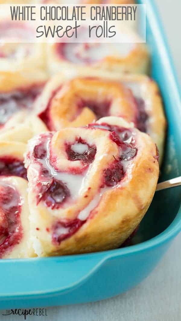 white chocolate cranberry sweet rolls in bright blue pan with one roll lifted up