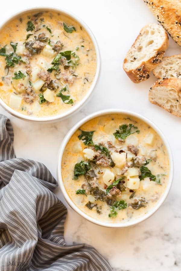 two bowls of zuppa toscana on white background with bread