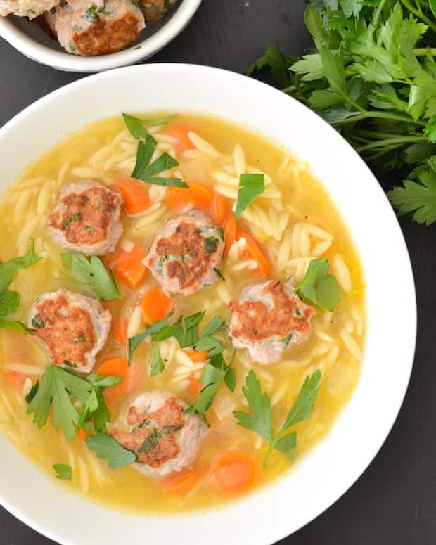 lemon orzo soup with turkey meatballs in white bowl with carrots and parsley