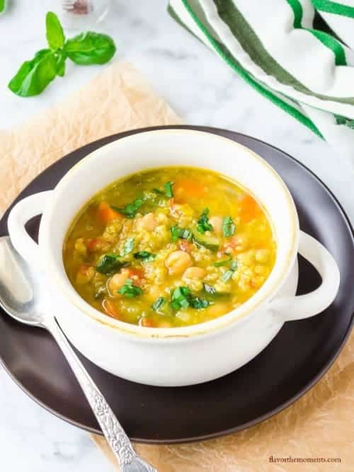 saffron vegetable soup with quinoa in white bowl on top of black plate