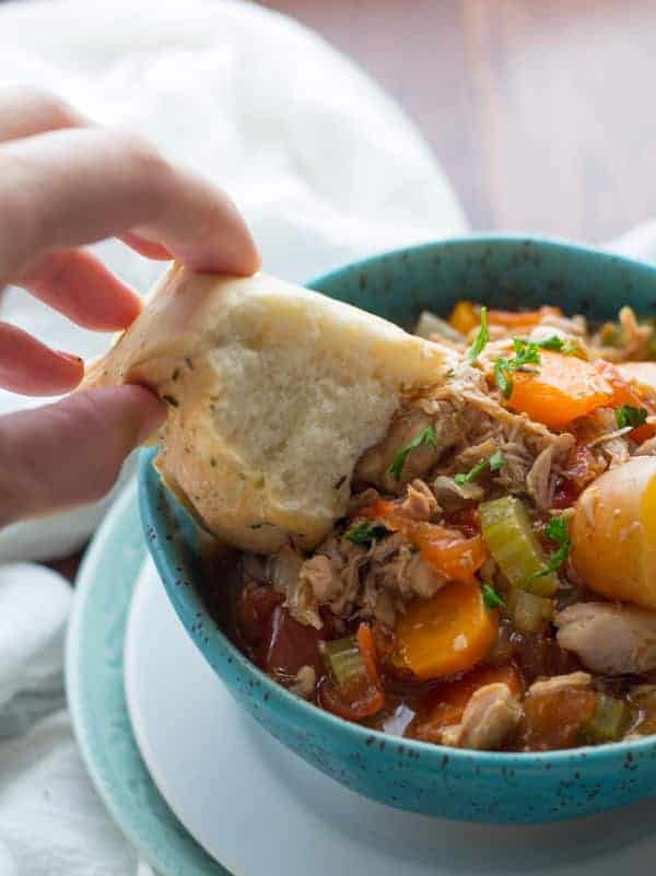 slow cooker tuscan chicken stew in bright blue bowl with crusty bread dipping in