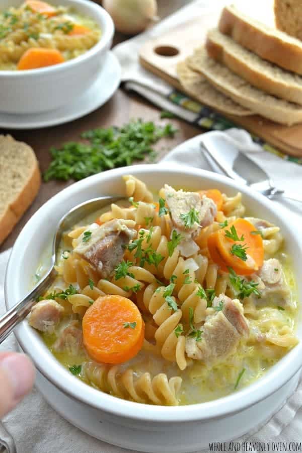 creamy chicken noodle soup in white bowl piled high with noodles chicken and carrots