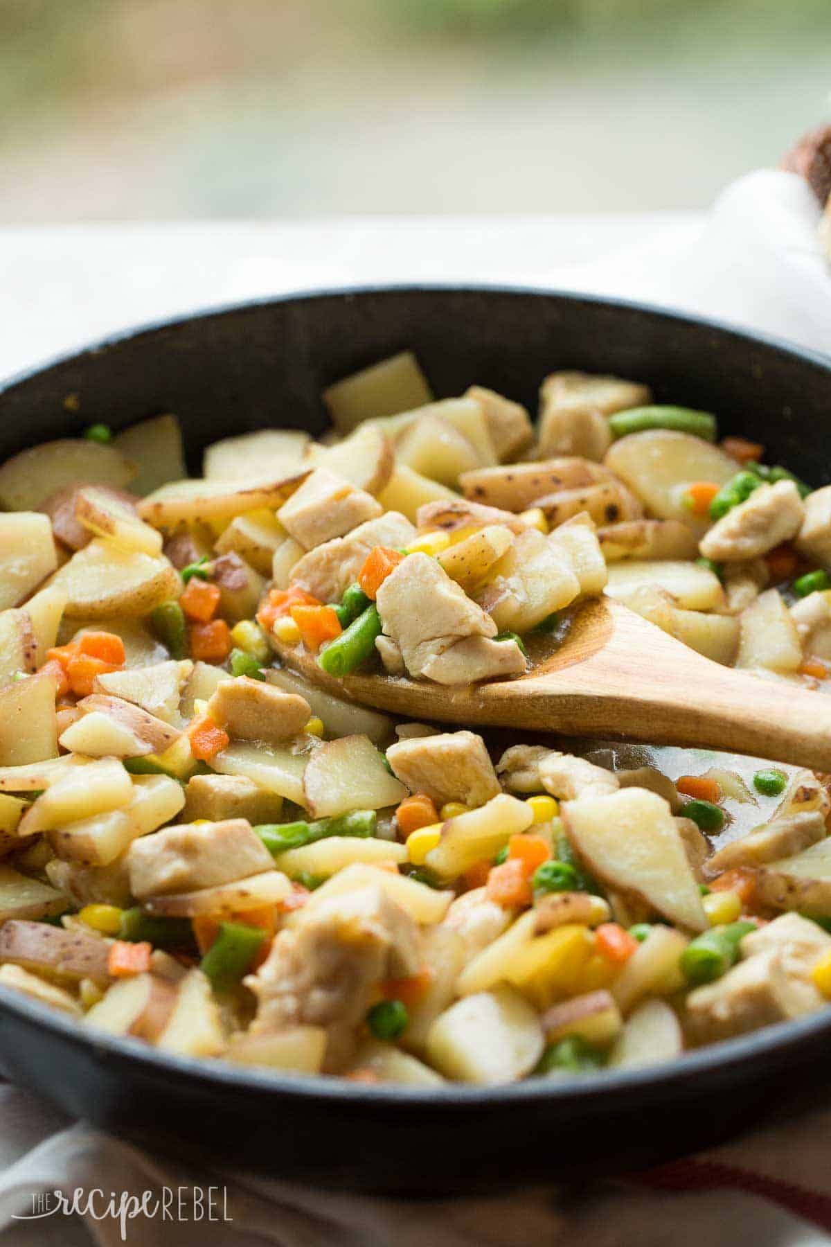 close up image of chicken stew in black skillet with wooden spoon scooping