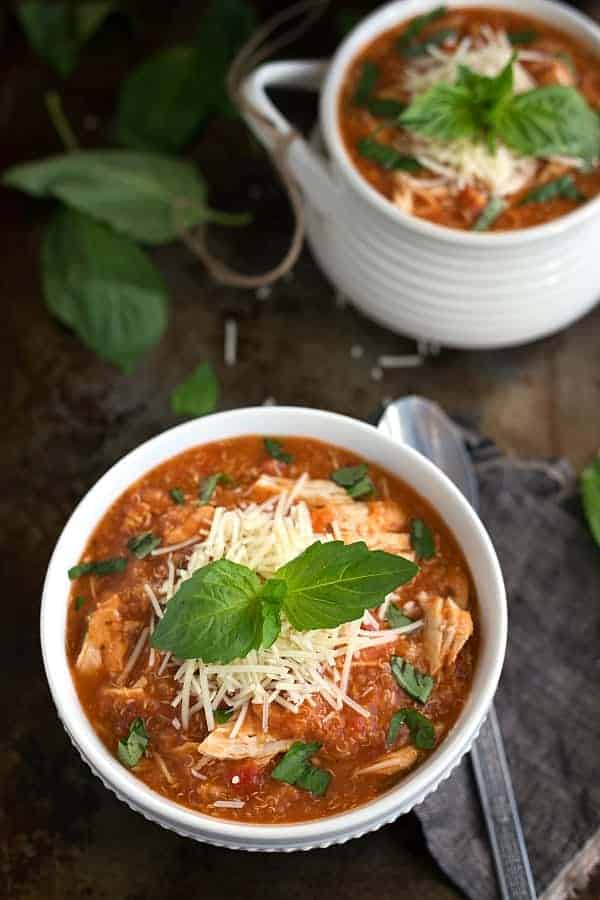 slow cooker chicken parmesan quinoa soup in white bowl topped with parmesan cheese and basil