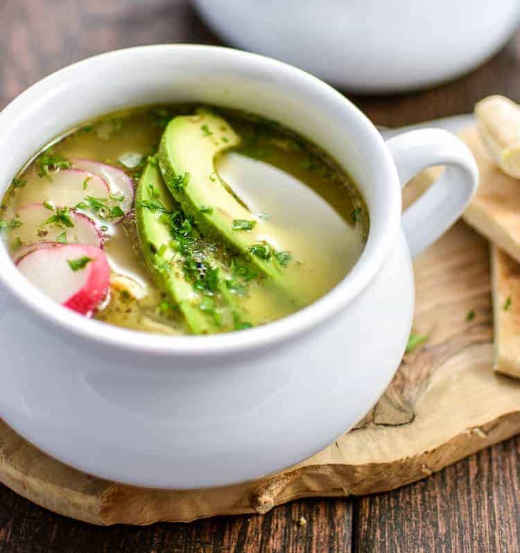 chicken posole verde soup in white bowl with avocado slices and radishes