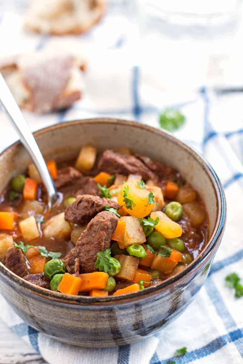 simple beef stew in brown bowl with spoon stuck in soup