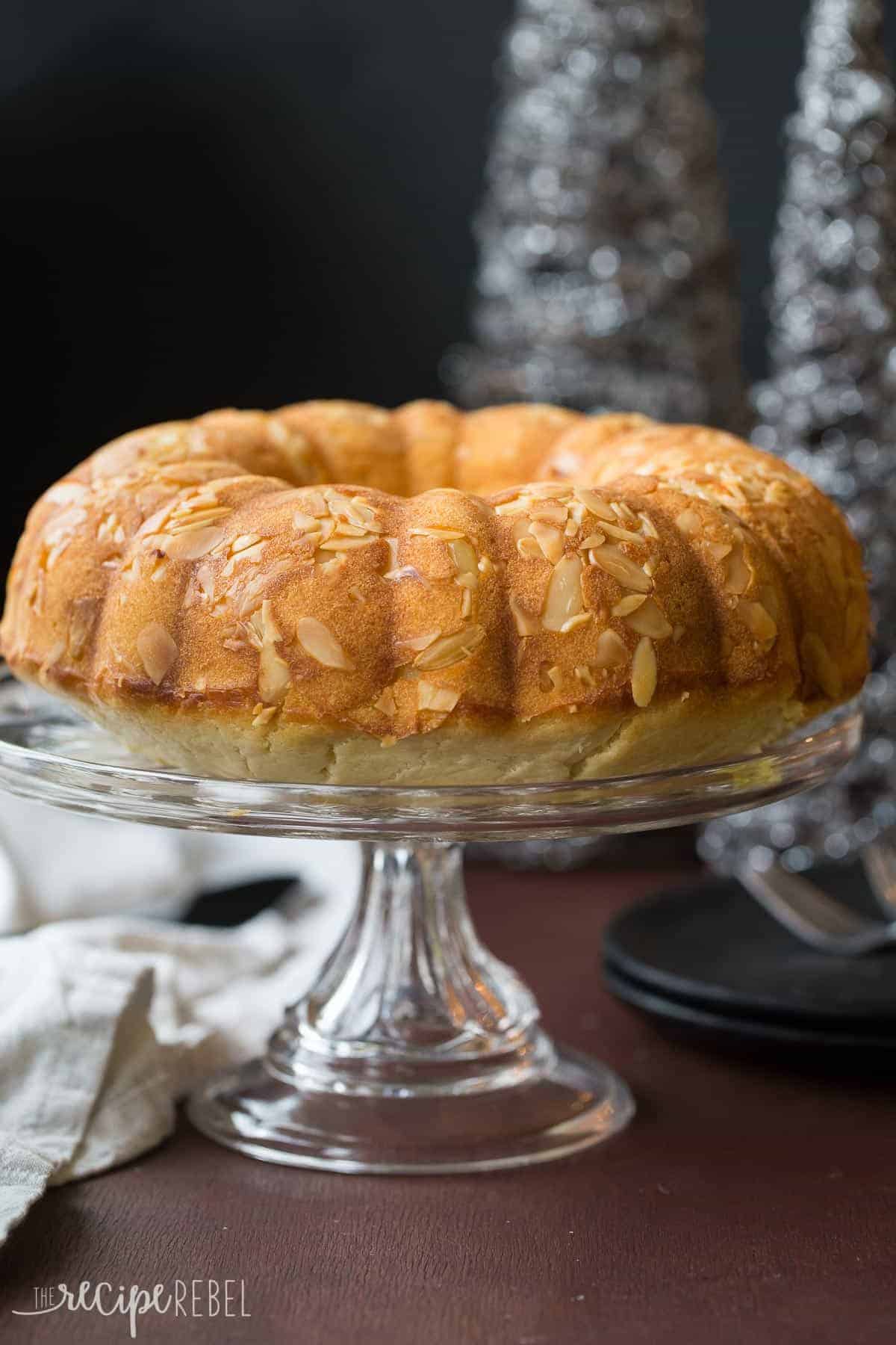 whole almond pound cake on glass cake plate with almond slivers baked into the top