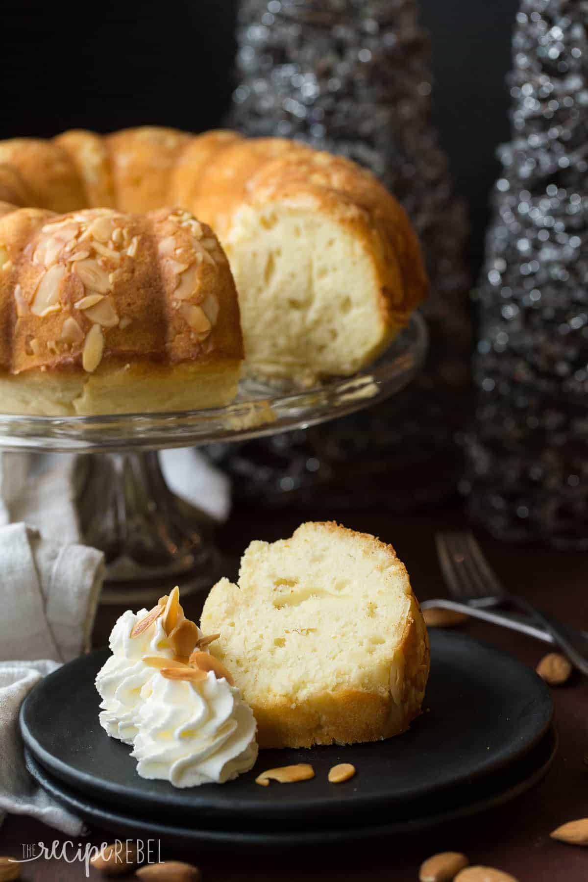 slice of almond pound cake on black plate with whipped cream swirls and toasted almonds