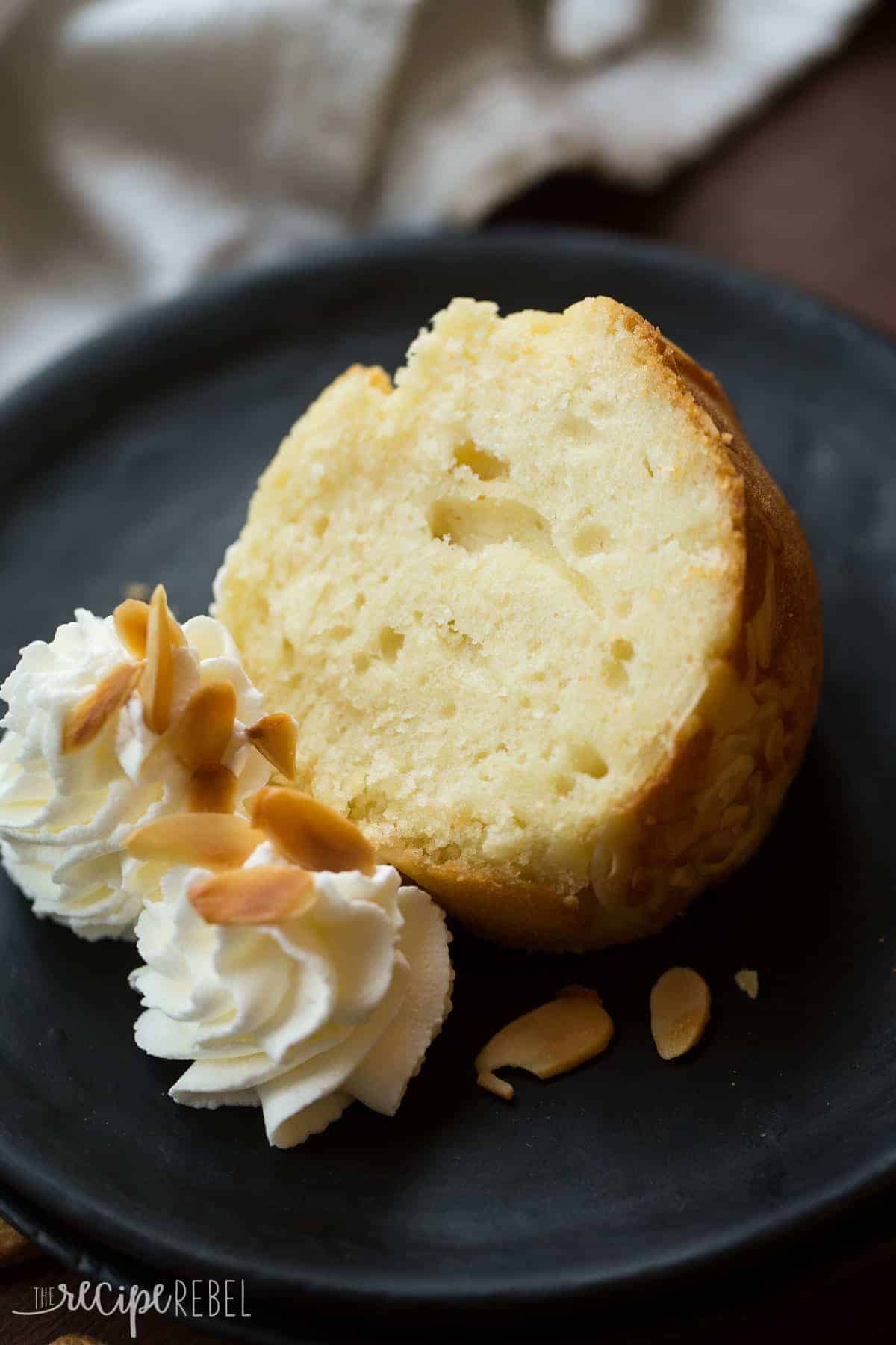 close up image of slice of almond pound cake on black plate with whipped cream