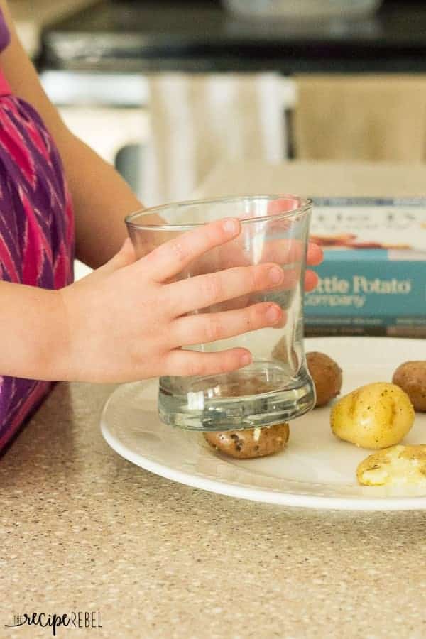 little girl hands smashing little potatoes on a plate