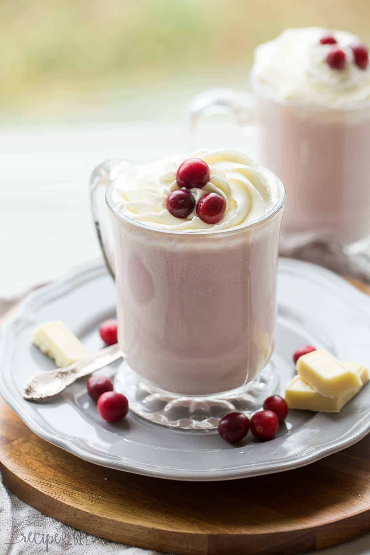 mug of cranberry white hot chocolate on a grey plate with fresh cranberries and white chocolate around