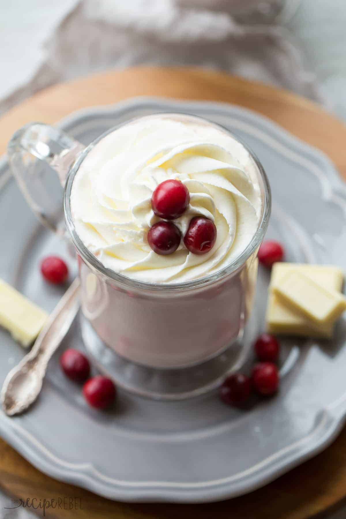 close up overhead image of glass of cranberry white hot chocolate with whipped cream and cranberries on top