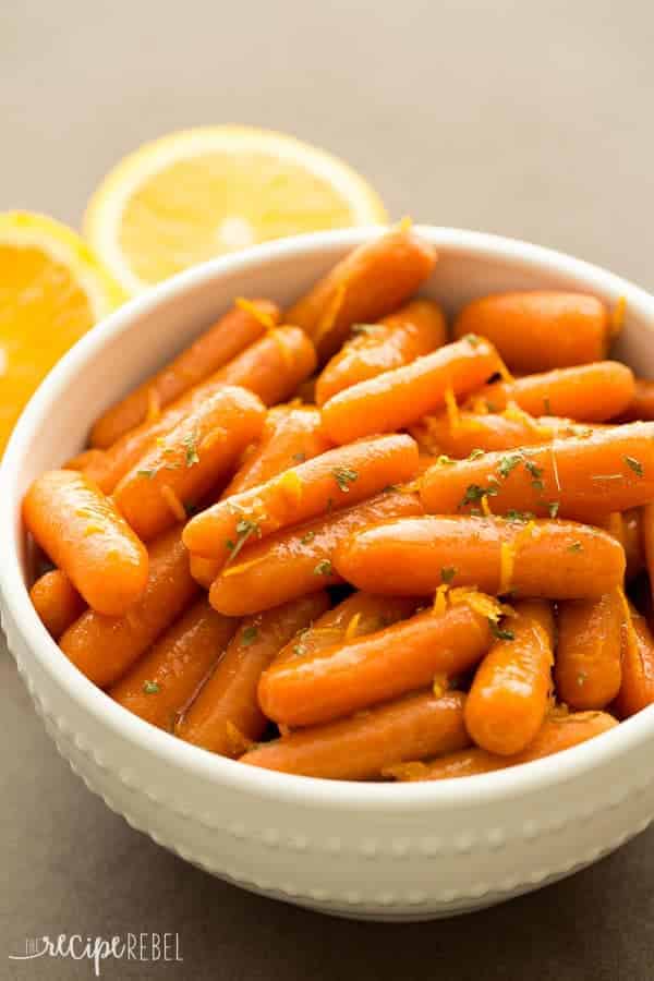 white bowl with slow cooker honey orange glazed carrots and fresh oranges behind