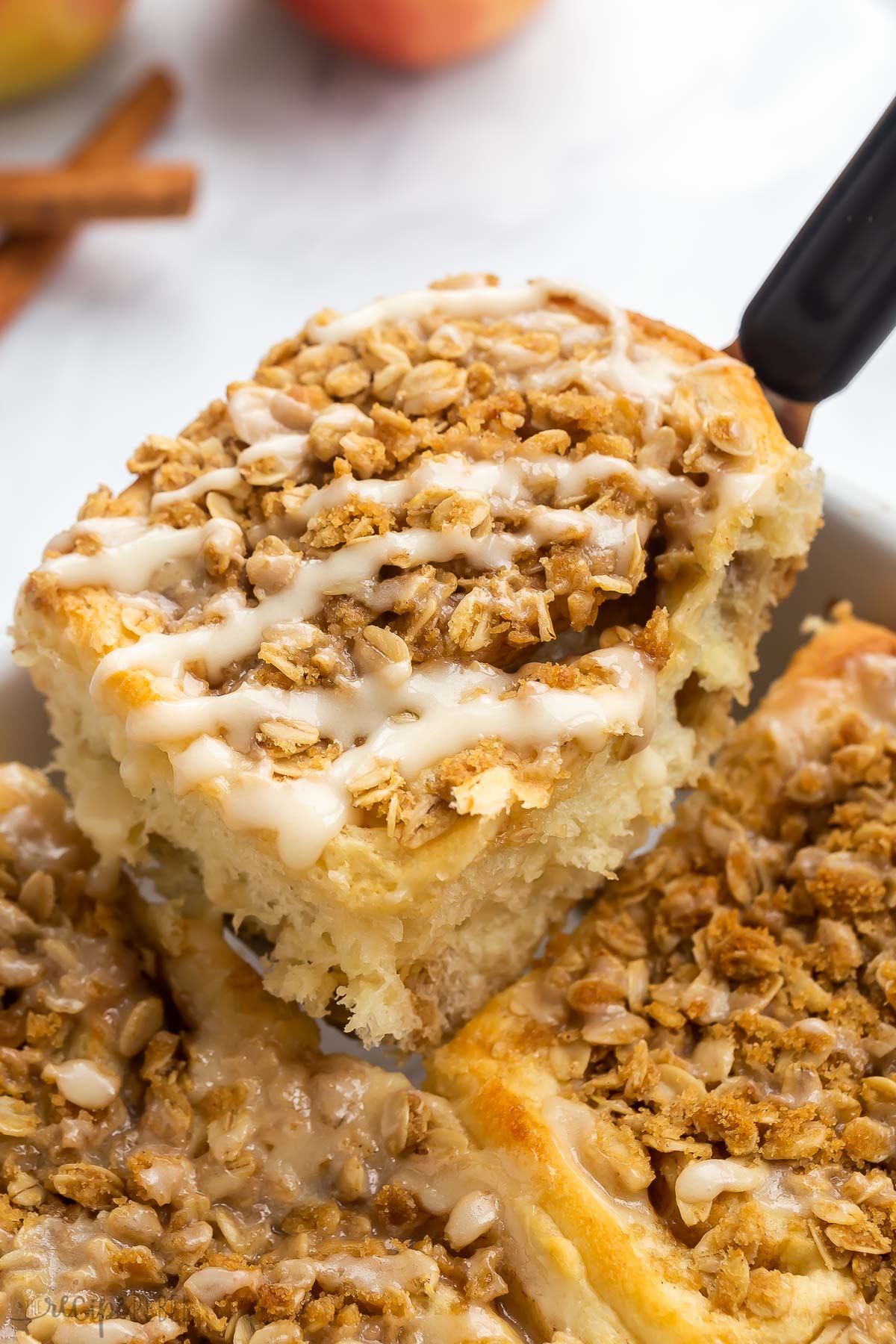 metal spatula lifting one apple cinnamon roll out of the pan.