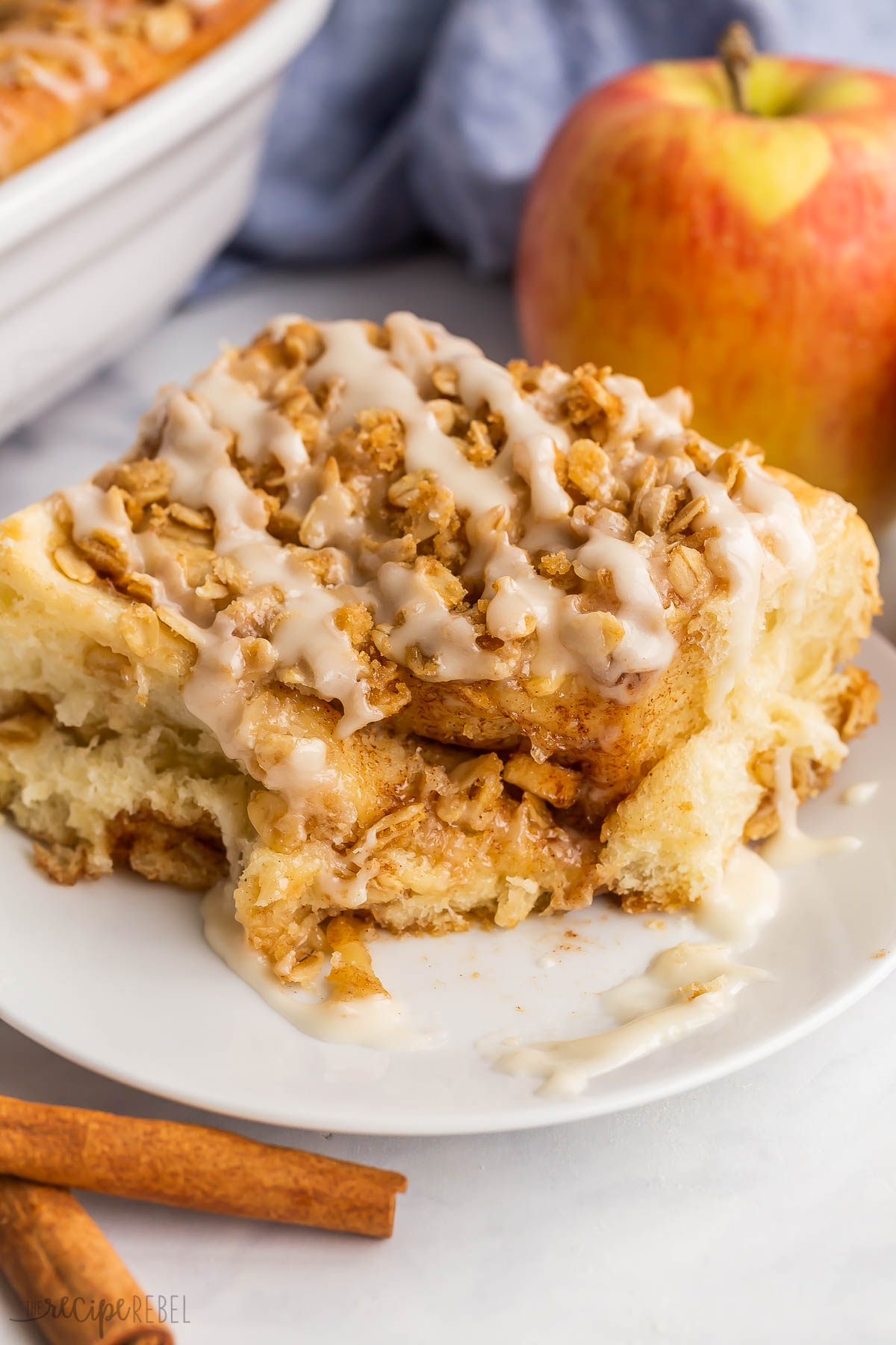 bite taken out of apple crisp cinnamon bun on white plate.