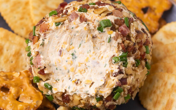 cheese ball on a blue plate with some scooped onto a cracker.