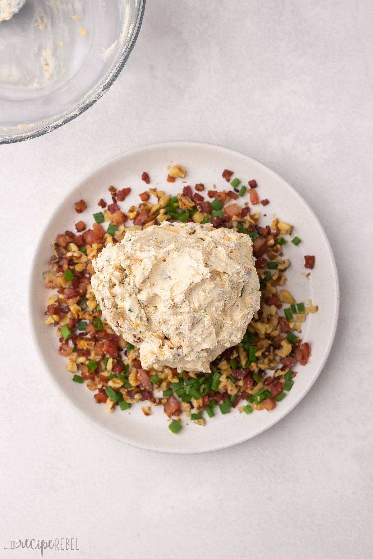 cheese ball on a plate with extra bacon nuts and green onions to cover.