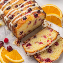 side angle of whole cranberry orange bread with two slices cut and orange slices and cranberries on the side.