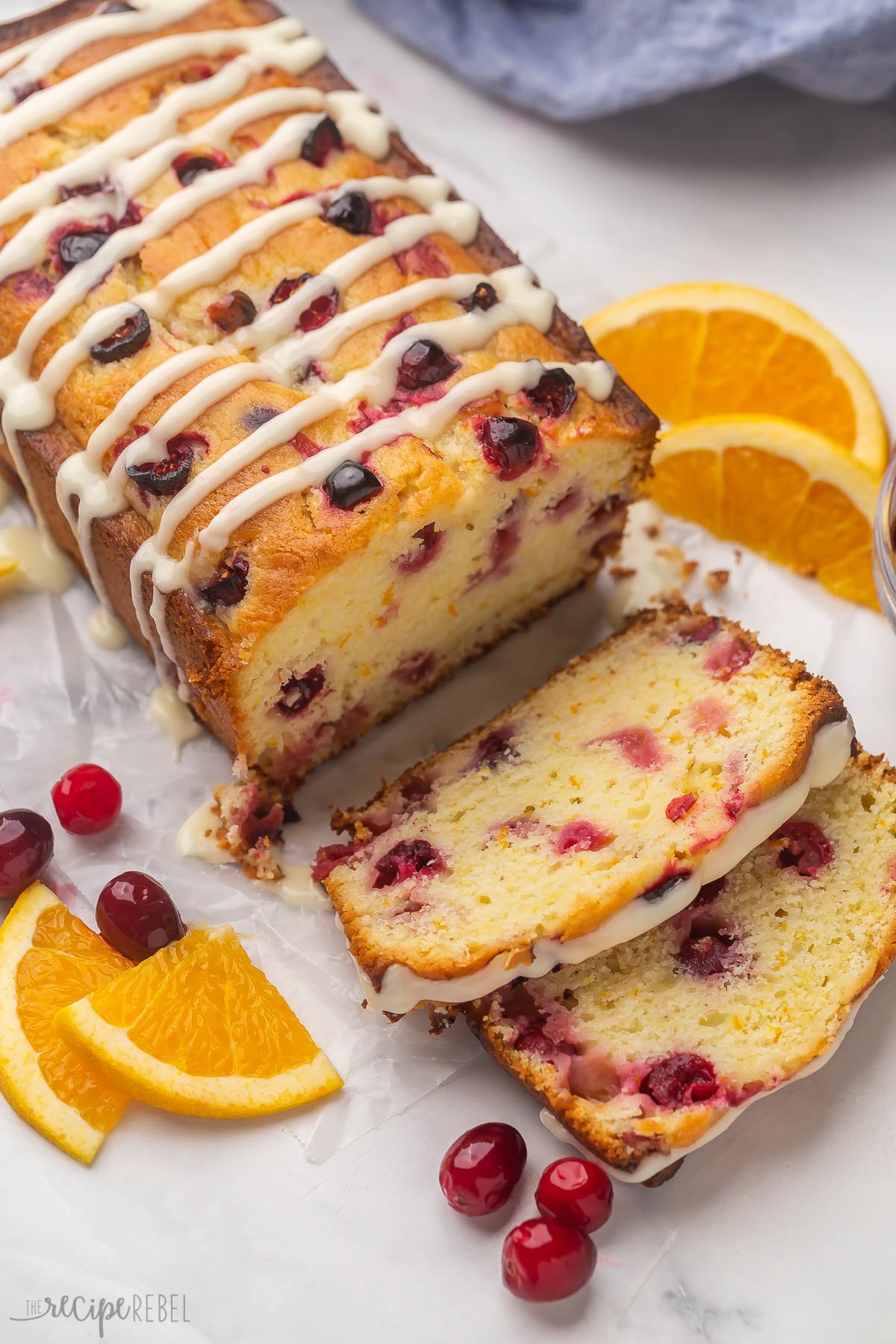 side angle of whole cranberry orange bread with two slices cut and orange slices and cranberries on the side.