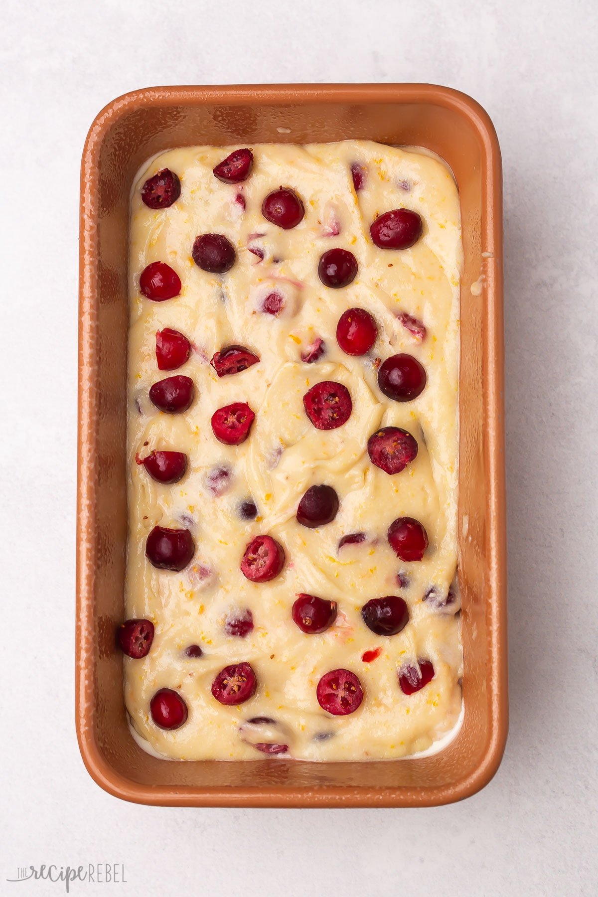 orange cranberry bread batter in loaf pan with fresh cranberries on top.