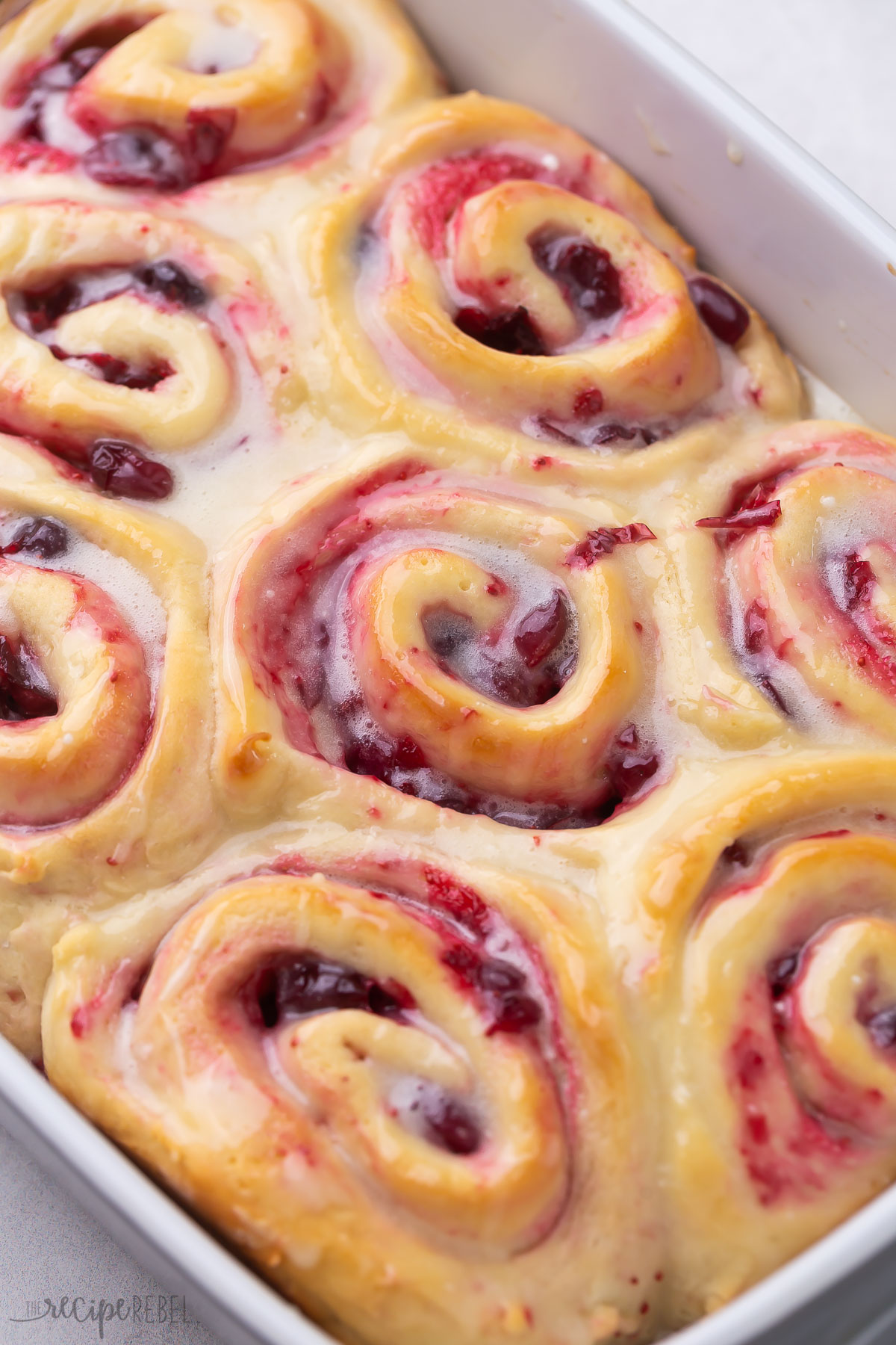 close up image of cranberry rolls with glaze in pan.