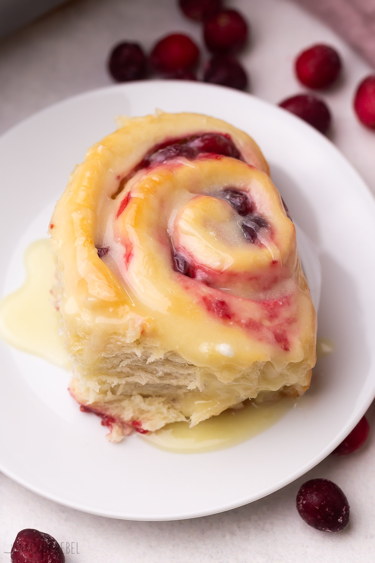 close up image of one cranberry roll on white plate with white chocolate glaze.
