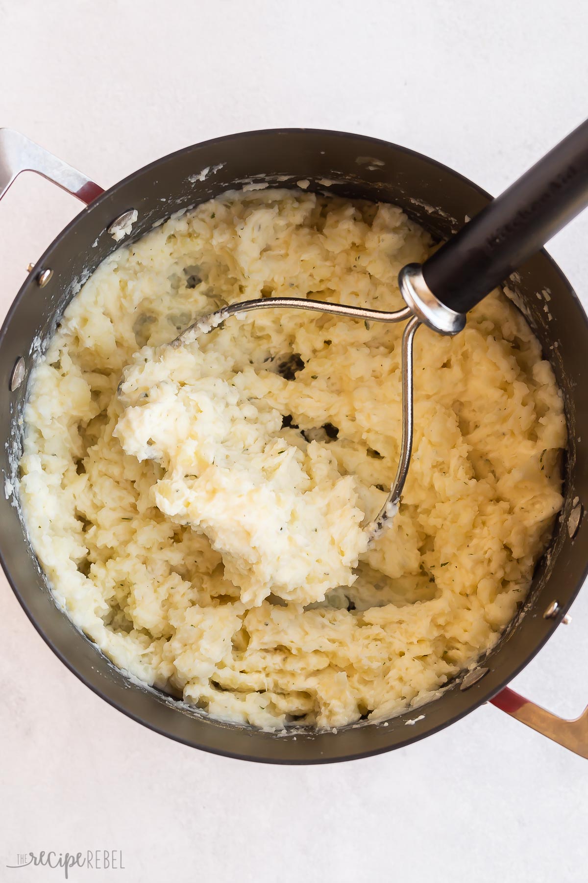 potato masher mashing potatoes in pot.