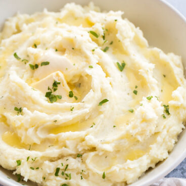 mashed potatoes spread in bowl with melted butter and parsley.