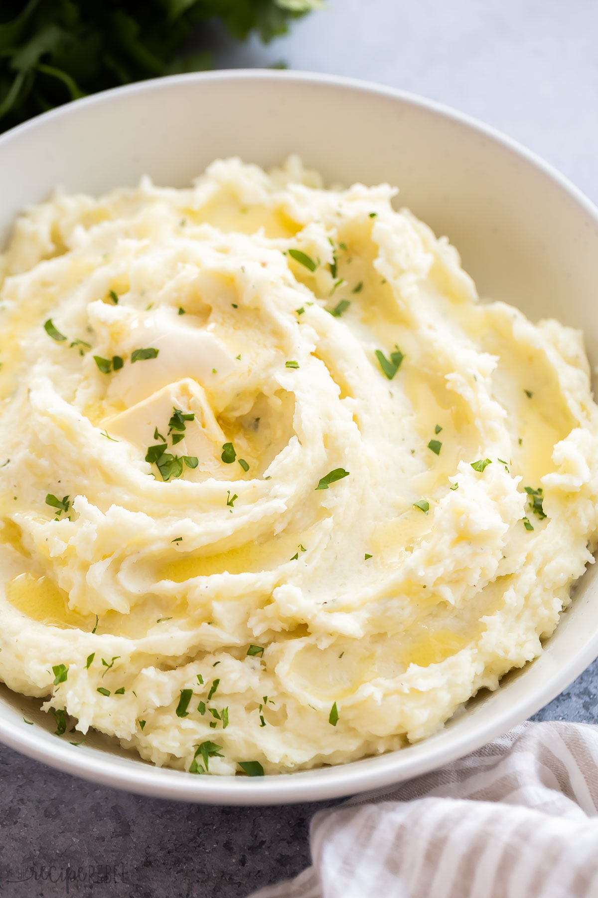 mashed potatoes spread in bowl with melted butter and parsley.