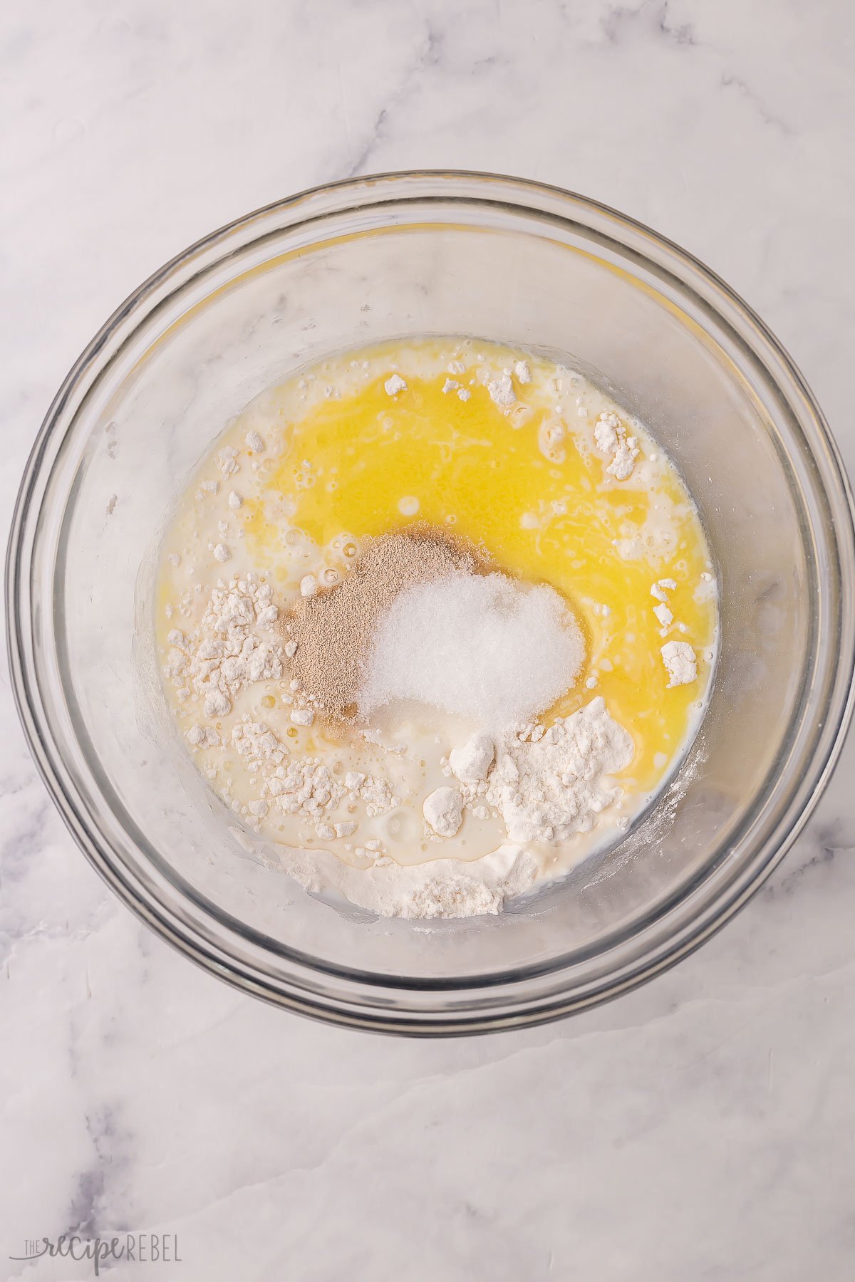 flour yeast sugar milk and melted butter in a glass bowl ready to mix.