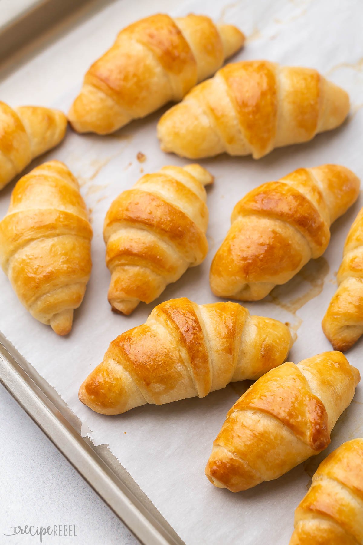 These Crescent Rolls are a made-from-scratch classic! They're light, fluffy, buttery, flaky, and take just 15 minutes to prep! #baking #bread | bread baking | homemade bread | homemade rolls | dinner rolls | crescent roll recipe | christmas dinner multiple crescent rolls on a baking sheet with parchment paper.