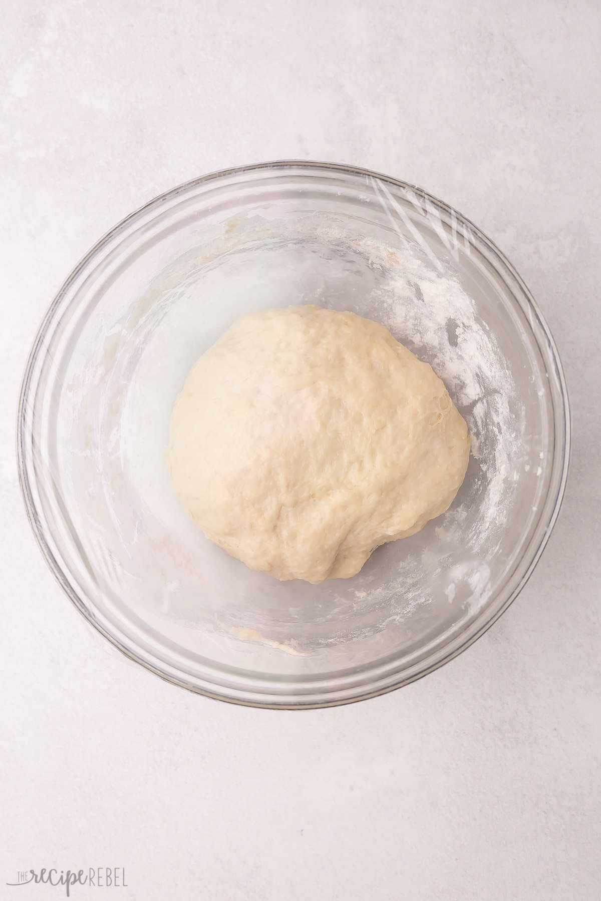 ball of dough in glass bowl covered in plastic wrap.