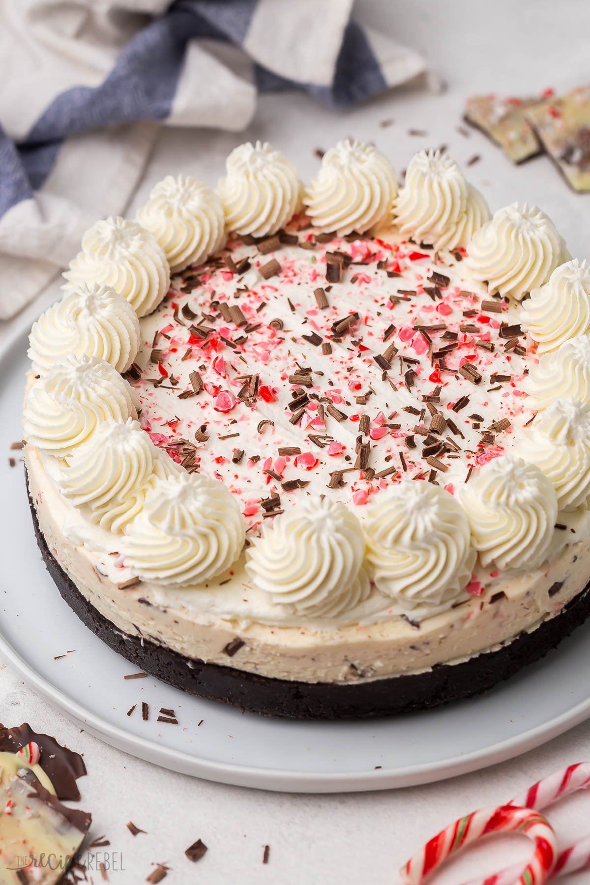 close up image of no bake peppermint bark cheesecake with whipped cream crushed candy canes and chocolate shavings.