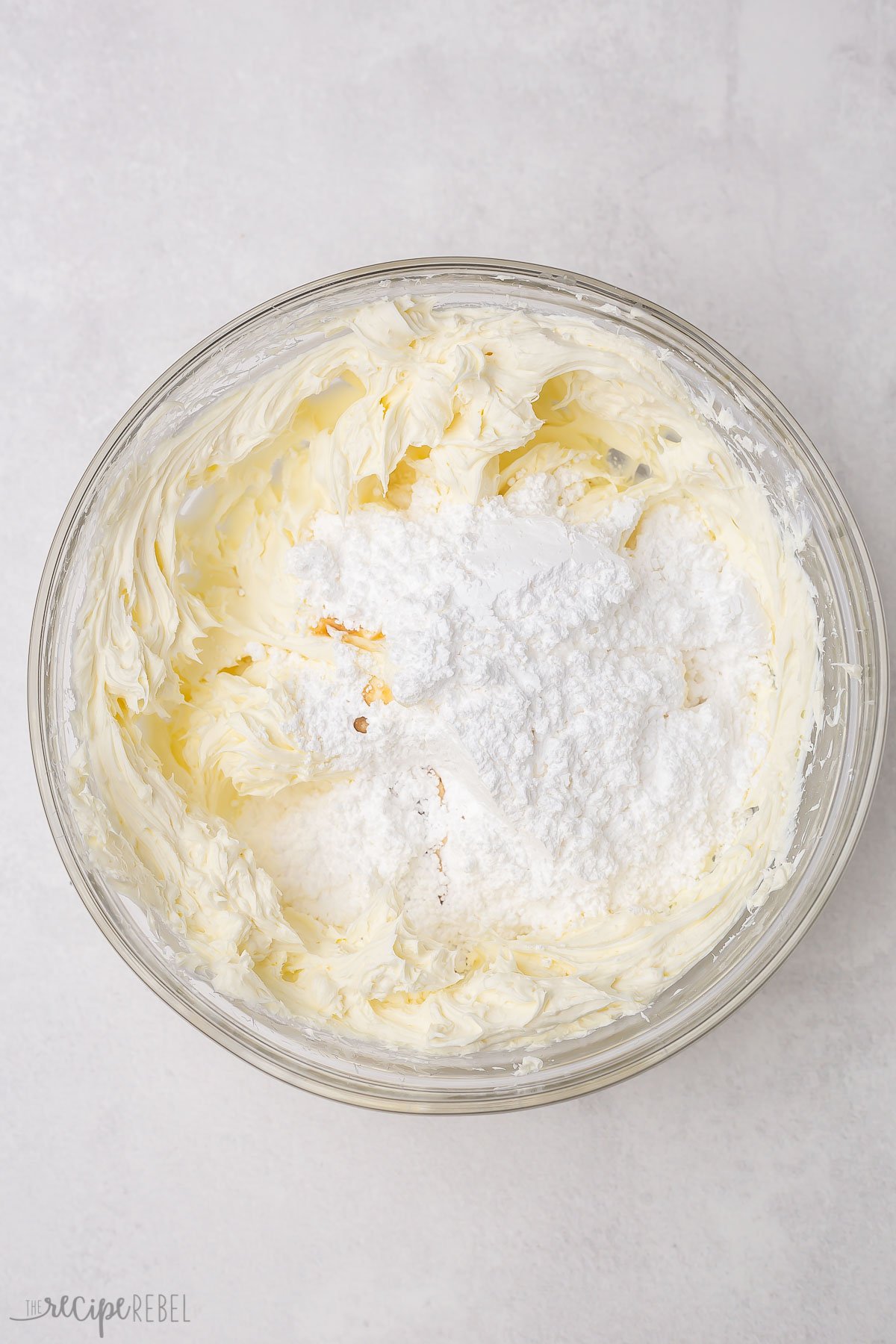 powdered sugar added to cream cheese in glass bowl.