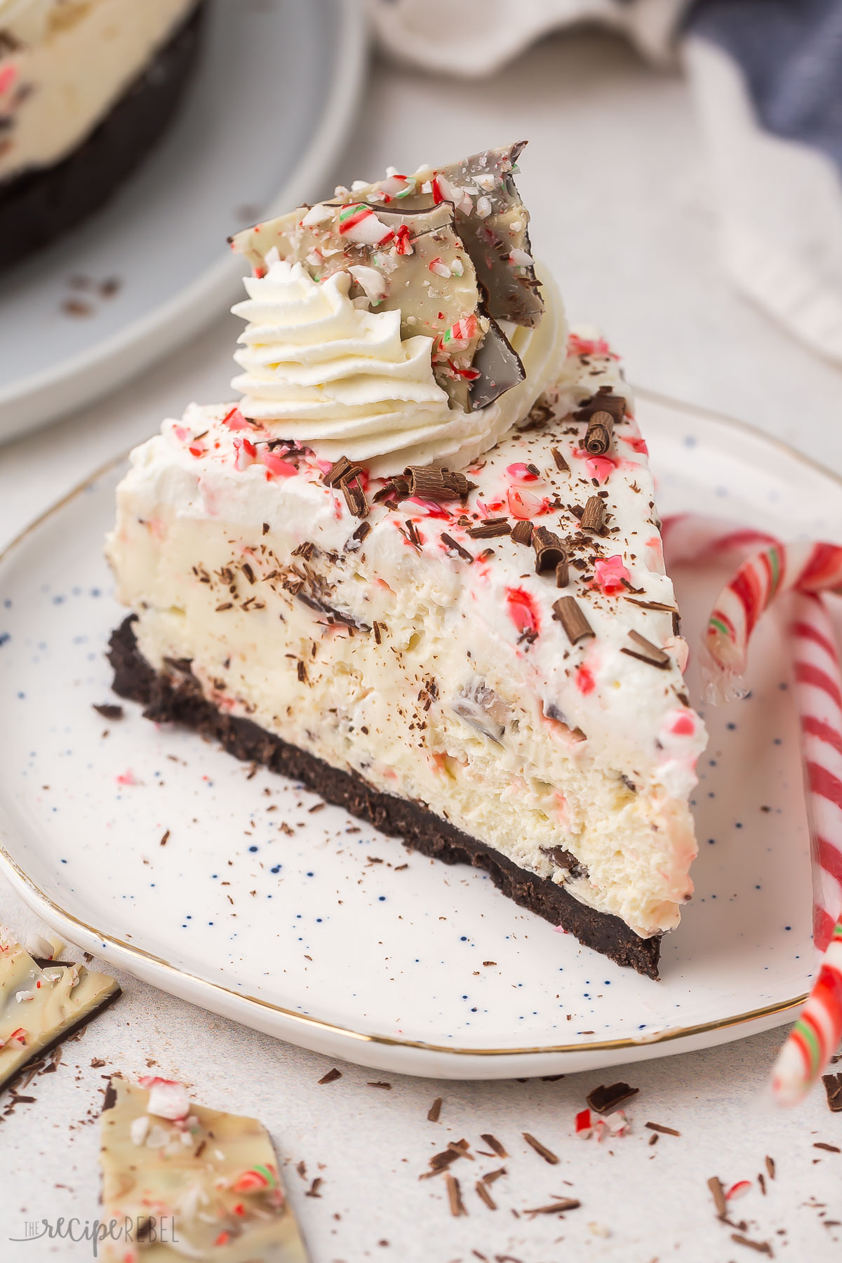 one slice of peppermint bark cheesecake on a white plate with candy canes.