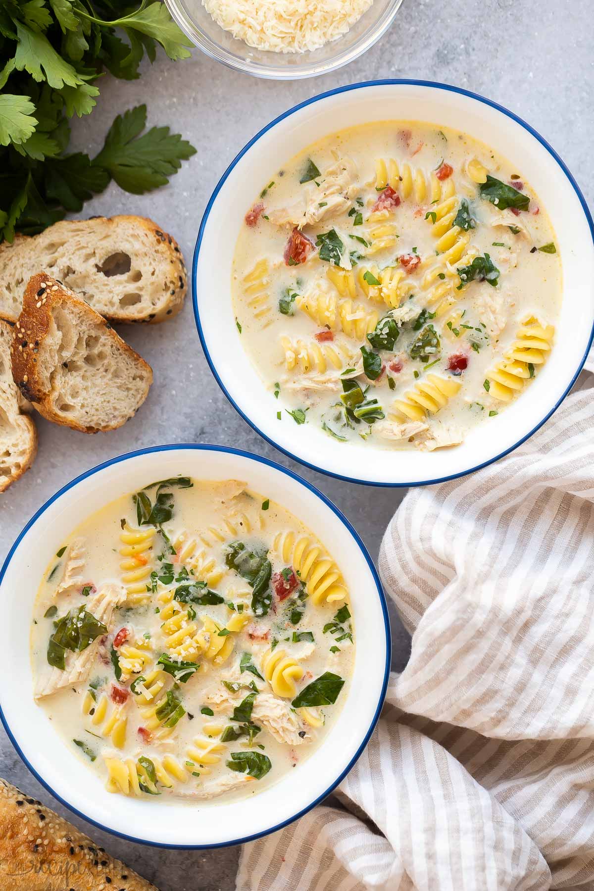 two bowls of italian chicken noodle soup on grey background with bread on the side.