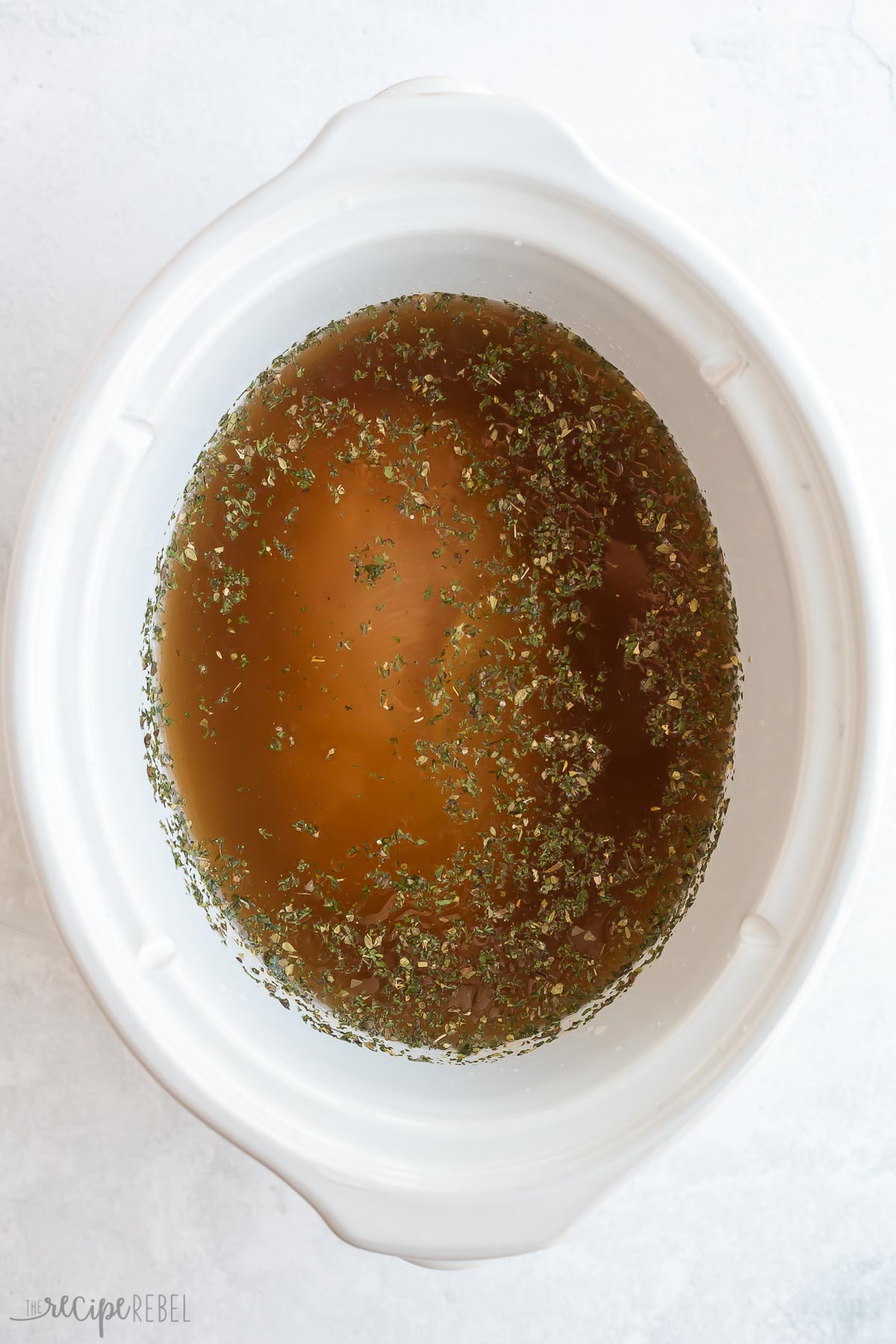 chicken broth and seasonings in slow cooker ready to cook.